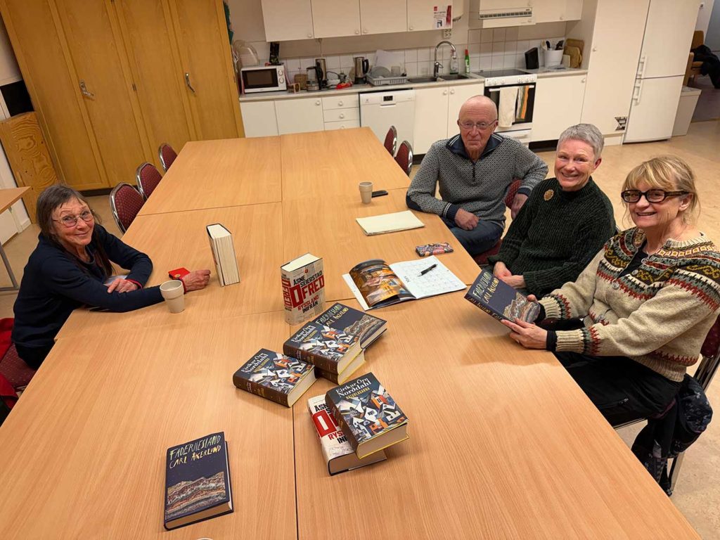 Fyra personer sitter vid ett stort bord. På bordet ligger böcker. Alla fyra tittar mot kameran och ler. 