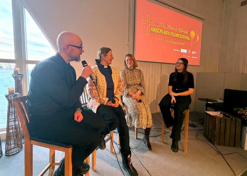 Fyra personer, en man och tre kvinnor, sitter på höga pallar bredvid varandra. Mannen håller en mikrofon nära munnen, kvinnorna skrattar. Bakom dem på en stor skärm på väggen står texten Tro, Film och Kärlek, Arjeplogs Filmfestival 13-15 februari 2026.