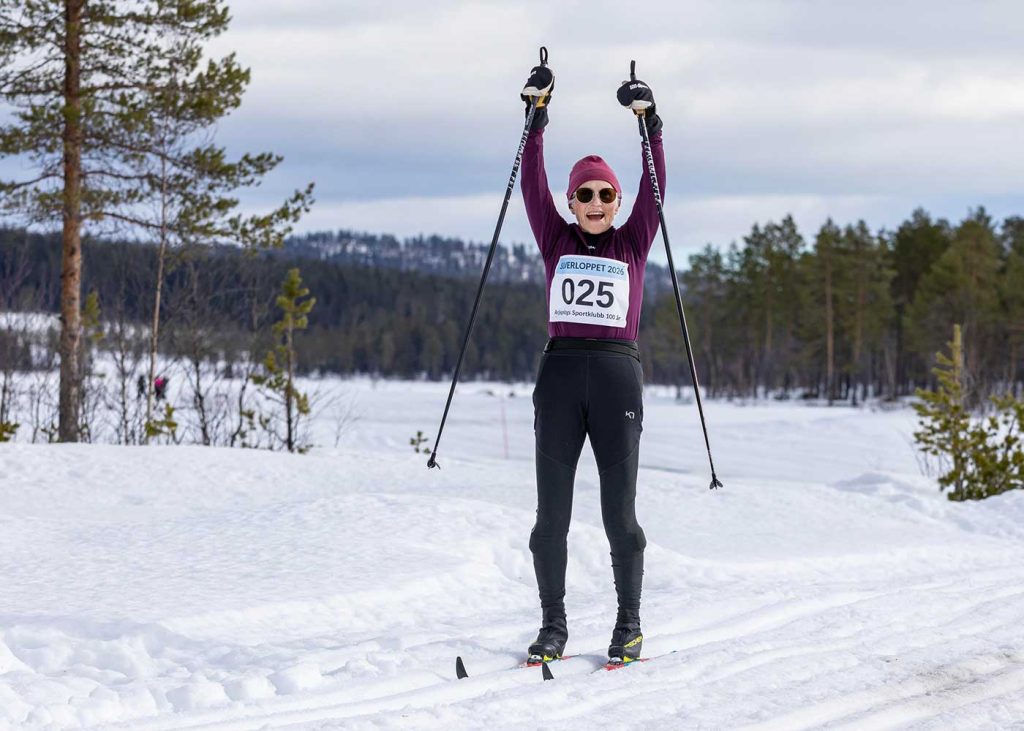 En väldigt glad kvinna i skidspåret. Hon höjer sina armar i luften och tittar mot fotografen.