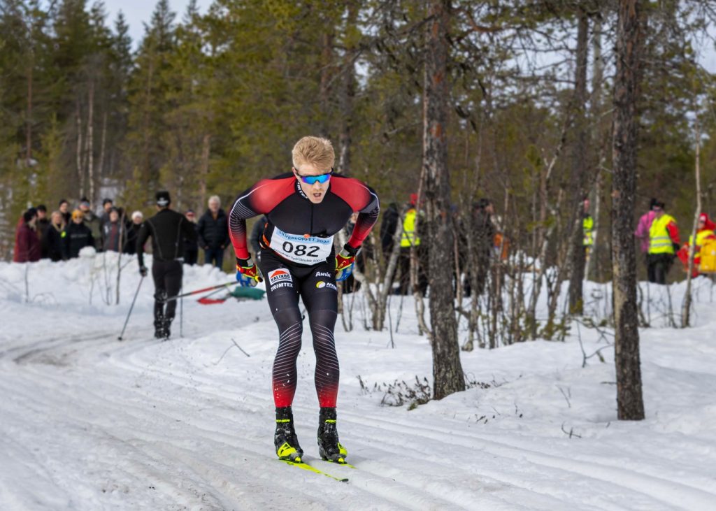 En skidåkare på väg mot fotografen. I bakgrunden träd och publik.