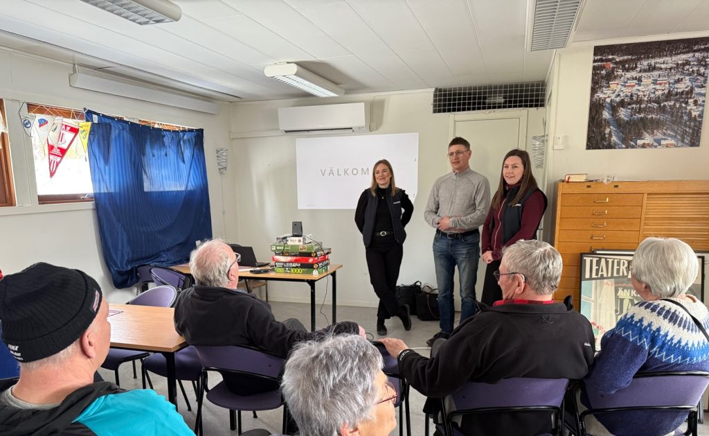 Bild inifrån möteslokal. I förgrunden syns några ur publiken, bakifrån. Alla vända mot två kvinnor och en man. Mannen står mellan kvinnorna. Alla tre ser glada ut.