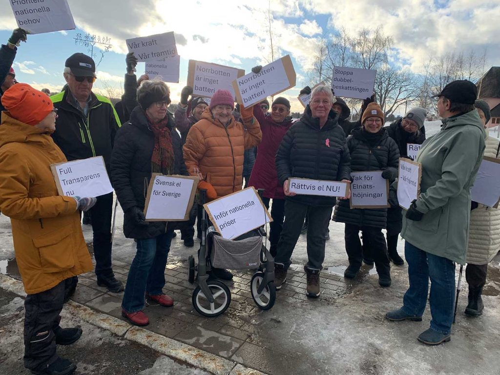 En grupp människor iförda vinterkläder och utrustade med skyltar där man bland annat kan läsa ”Svensk el för Sverige”, ”Inför nationella priser” , ”Vår kraft Vår framtid” och ”Norrbotten är inget batteri”. De allra flesta som syns i bild är kvinnor. Inga ungdomar syns. Människorna i gruppen ser taggade ut, de håller upp skyltarna högt och riktar dem mot fotografen.