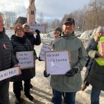 Kvinnor med skyltar som protesterar mot elpriserna. I bakgrunden Arjeplogs kyrka.